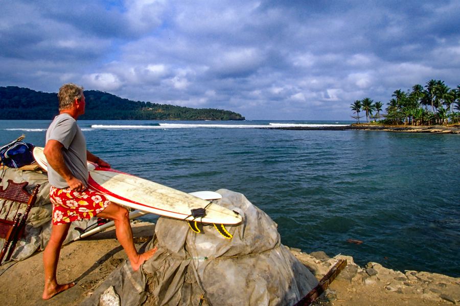 Surfer with board on the rocky shoreline, São Tomé