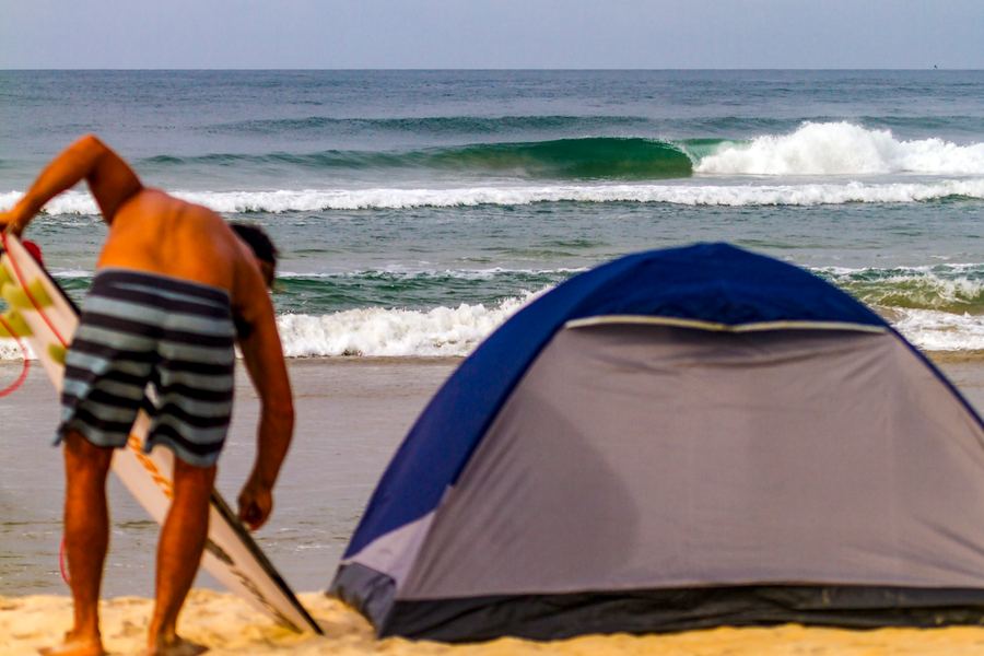 Surfer beside a camp tent on the beach, Sierra Leone